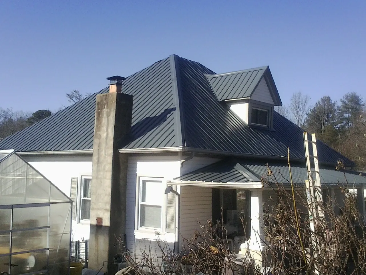 Dark blue standing seam metal roof on a white farmhouse with dormer — Slate & Tile Roof Repair by Roofing Brothers in Old Bridge