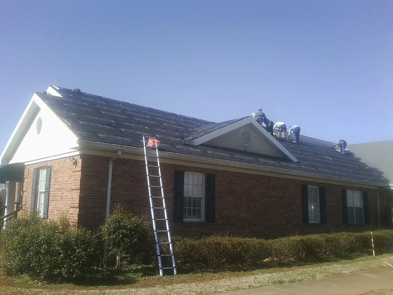 Crew tearing shingles off a brick ranch roof with a ladder set — Emergency Roof Repair work by our crew in Old Bridge