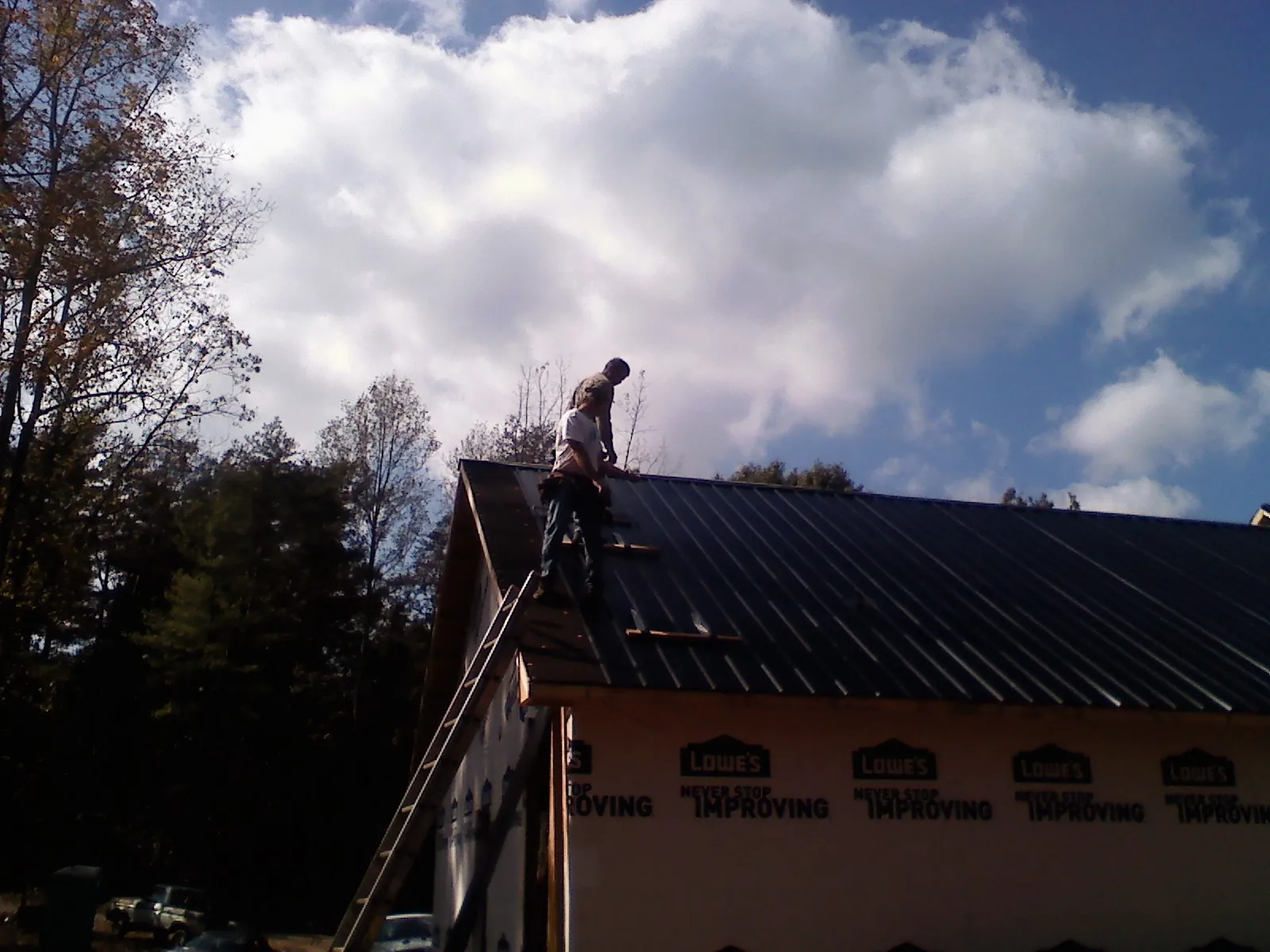 Roofer fastening dark metal panels high against a cloudy sky, from a Roof Inspection job in Old Bridge
