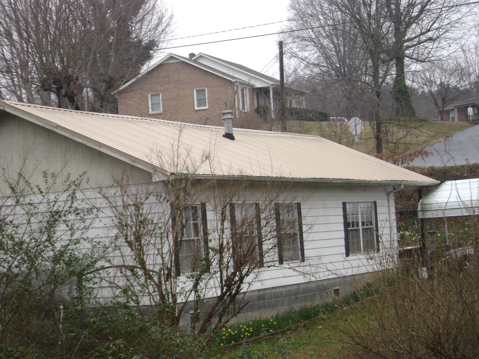 Tan metal roof on a white sided house set into a hillside — Commercial Roofing by Roofing Brothers in Old Bridge